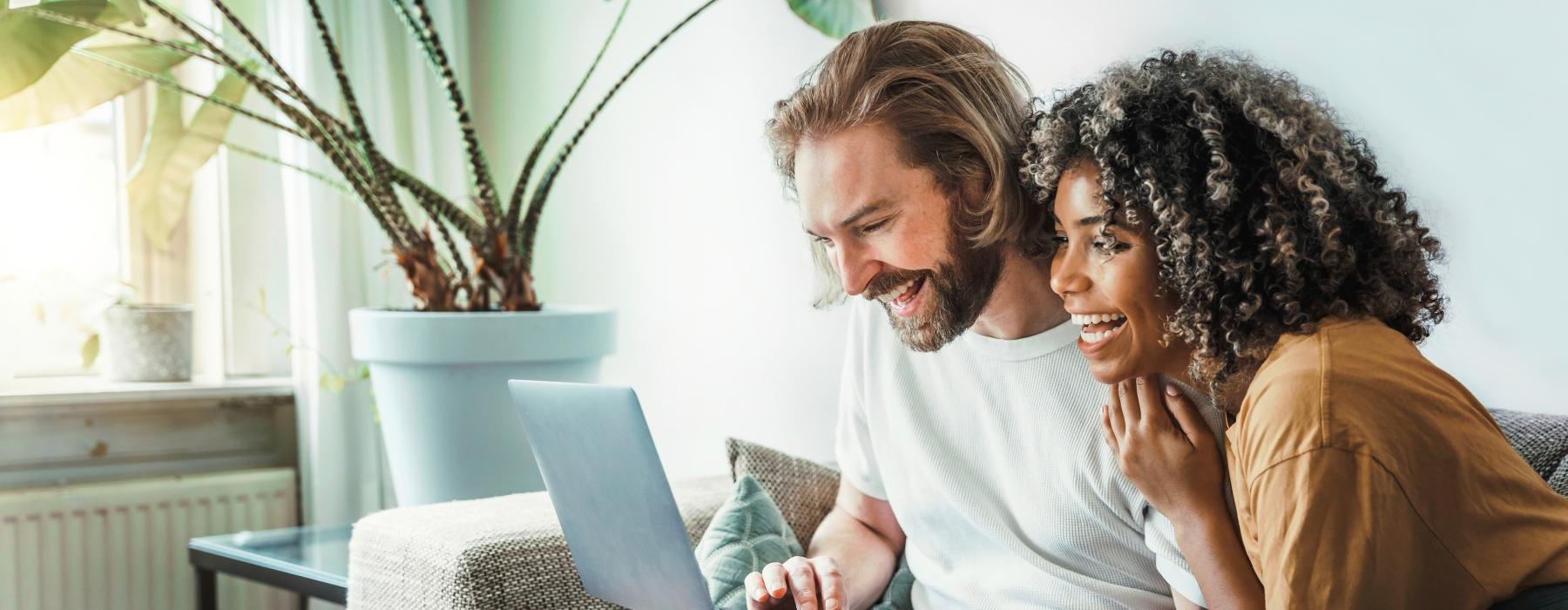 a man and a woman sitting on a couch looking at a laptop